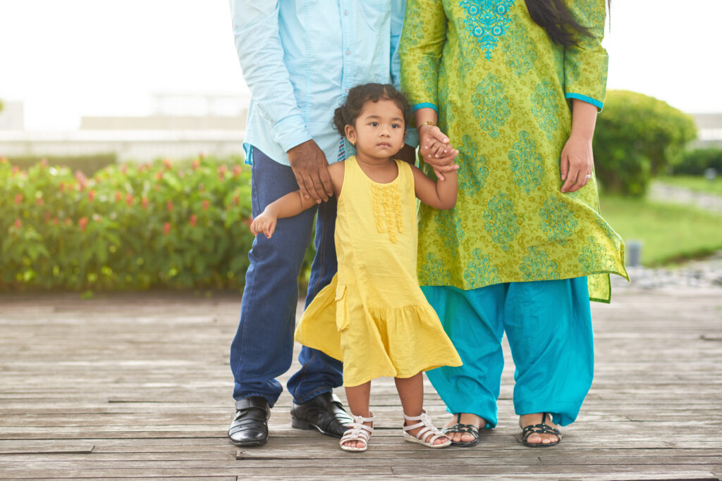 Full length portrait of cute little girl wearing yellow dress looking away thoughtfully while having walk with her parents in summer park